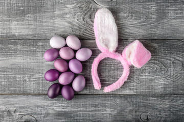 Easter eggs in a fashionable coloring on a gray wooden background with a female hoop with Easter bunny ears