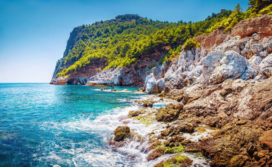 Scenic seascape of sea with stones and rocks on beach and mountains with green forest on peak. Tropical summer nature landscape of Turkey on sunny summer day. Hiking and travel adventure outdoors