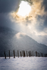 Winterlandschaft: Beschneites Feld und aus den Wolken herausbrechende Sonne
