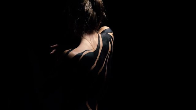 The girl in black body art stands with her back to the camera and moves like a snake