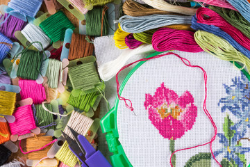 The process of cross-stitch. Canvas on hoops, needles, embroidery floss and pattern.