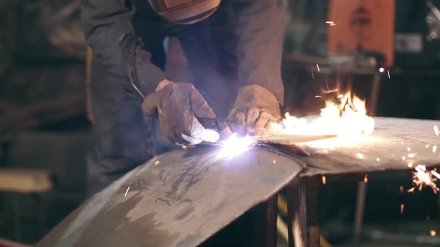 Male worker in protective gloves and workwear is cutting off metal piece with oxy acetylene cutting torch at a factory. Slow motion footage.