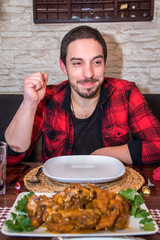 Abendessen Junger Mann in Karohemd schaut auf Teller, davor Lammbraten mit Soße