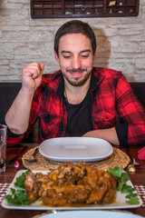 Abendessen Junger Mann in Karohemd schaut auf Teller, davor Fleischgericht
