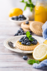 Shortbread homemade tartlet filled with lemon curd and fresh blueberries on rustic wooden background. Holiday food concept with copy space.