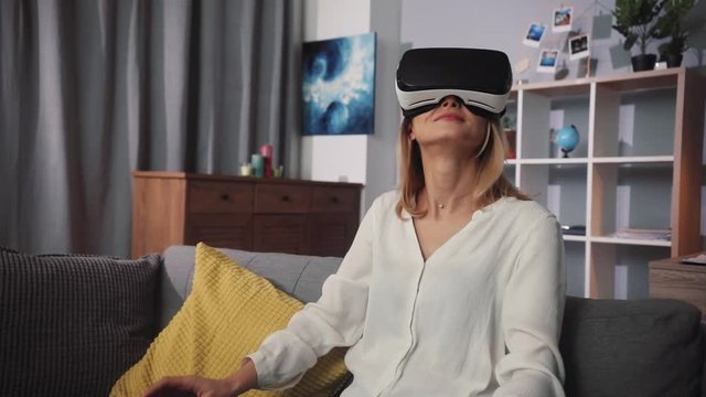 Young beautiful woman wearing virtual reality glasses waving his hands sit on the sofa at home feel happy smiling innovation looking entertainment gadget new tech visual game hipster slow motion