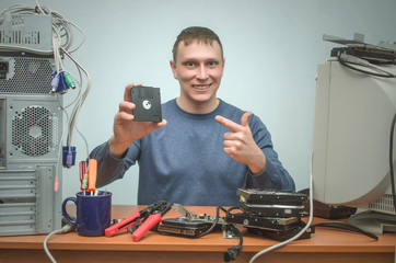 Computer technician engineer is holding in one hand a backup diskette disk and is showing on it by...