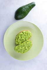 Avocado and sandwiches with avocado paste on white background, half of green avocado, copy space, sandwiches with pasta with avocado on a green plate, exotic fruits, vegan, diet food, mexican cuisine