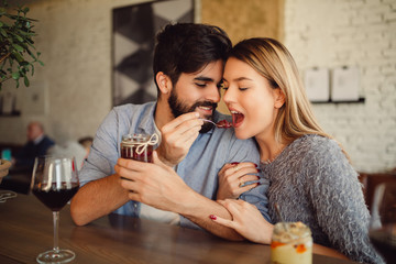 Handsome man feeding her girlfriend with cake in cafe. Couple celebrating anniversary, Valentine's day or International woman's day.