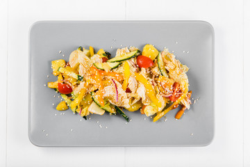 Vegetable salad with potatoes, cherry tomatoes, iceberg salad, Peking cabbage, bell pepper, cucumbers and red onion on a gray plate on a white background, top view