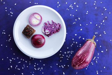 Purple cabbage, onions and beetroot on a white plate, vegetables in space, vegetables on the ultraviolet background, coarse salt, purple onions, purple eggplant on a dark blue background, pop art