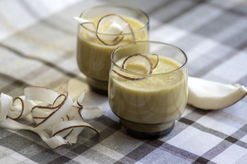 Pineapple smoothie with bananas, oatmeals and coconut milk, decorated with coconut chips, checkered tablecloth