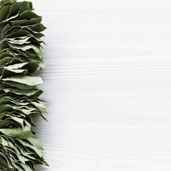 Bunch of bay leaves on white wooden background with space for text.
