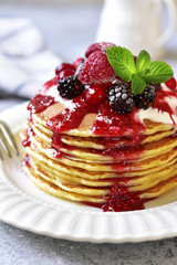 Stack of homemade delicious vanilla pancakes topped with sour cream,rasbberry syrup and berries.