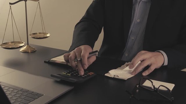 Justice and law concept.Male lawyer in the office working with calculator and bills with brass scale on wooden table