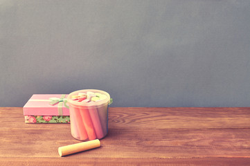 Color chalks and gift box on wooden background.