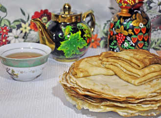 close-up of large and small pancakes lie on a plate, on the background of colorful samovar and kettle.