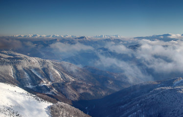 Forested Revucka dolina valley below Donovaly between Velka Fatra and Nizke Tatry ranges with low clouds and snow covered jagged Zapadne and Vysoke Tatry peaks on horizon Carpathians Slovakia Europe © nogreenabove2k