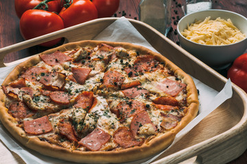 Pizza on wooden plate and food ingredients on kitchen table