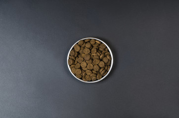 Dry dog pet food in bowl on blach chalkboard background top view. Pet feeding concept backgrounds with copy space. Photograph taken from above.