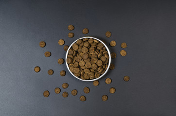 Dry dog pet food in bowl on blach chalkboard background top view. Pet feeding concept backgrounds with copy space. Photograph taken from above.