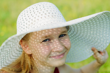 portrait of little girl with shadow on her face from white hat with large brim on green meadow background