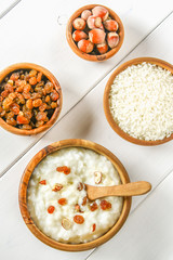 Rice milk porridge with nuts and raisins in wooden bowls on a white wooden table.