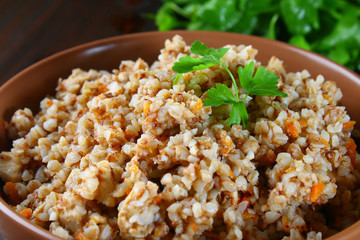 Boiled buckwheat in a bowl with pieces of chicken meat and cilantro on a brown wooden table.