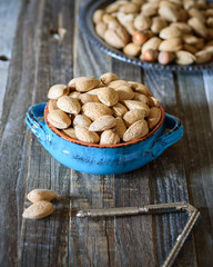 Nuts, whole almonds in a handmade vintage bowl on a wooden rutic background. Daylight.