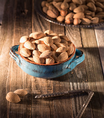 Nuts, whole almonds in a handmade vintage bowl on a wooden rustic background. In the dawn sunlight.