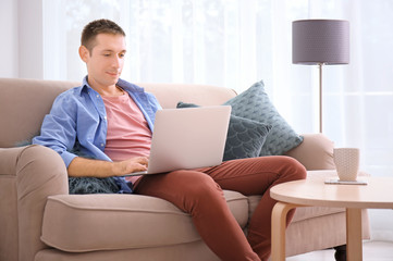 Fototapeta premium Young man in casual clothes using laptop at home