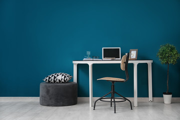 Comfortable home workplace with laptop on desk against color wall