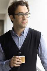 Portrait of a man standing having coffee looking away.