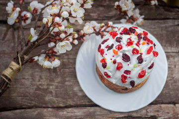 Naklejka premium Beautiful Easter cake stands on a wooden texture surface, near lies flowering apricot. place under text