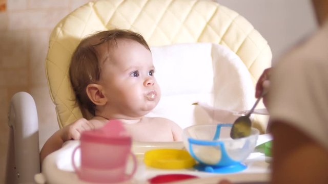 mom feeds baby from spoon. child eats at childrens table