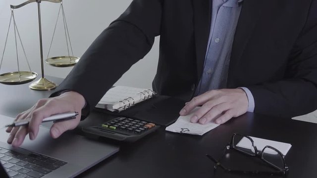 Justice and law concept.Male lawyer in the office working with calculator and bills with brass scale on wooden table
