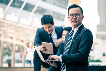 Group of  Asian business men working outdoor with computer devices. Technology and teamwork concept