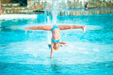 Happy little girl enjoy vacation in the swimming pool. Sporty kid making cartwheel on the edge of pool