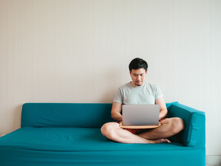Man is using  laptop on the sofa in his casual cloth.