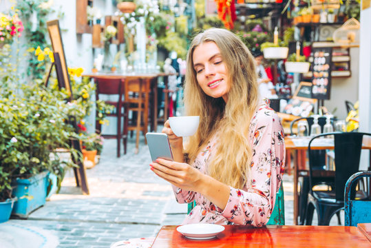 Beautiful woman is enjoying a cup of coffee and checking a mobile phone in the cafe