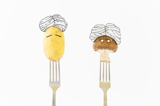 Potato and mushroom on white background with turban sitting as fakir on top of silver forks representing indian food.