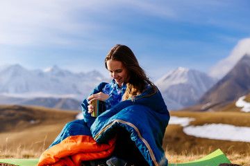 happy woman tourist sits and drinks tea against the background of mountains