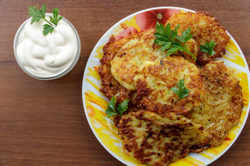 Homemade fried potato pancakes with sour cream on wooden table