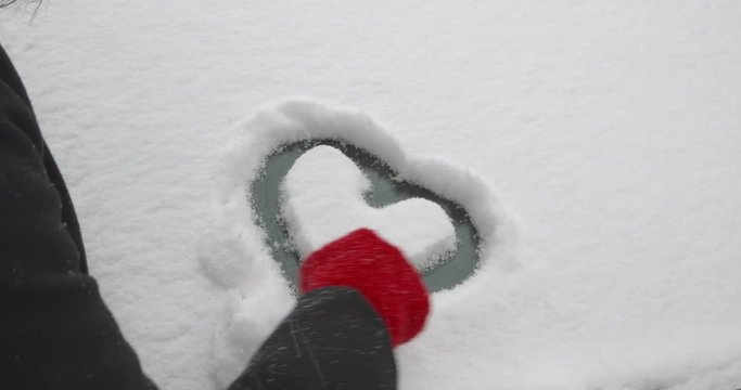A woman is refining an afore drawn heart shape on the windscreen of a snow-covered car - ProRes