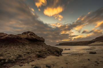 Beach on a Canarian island with dark clouds and big lava mountains at sunset