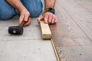 Man laying laminate by using hammer and wooden block