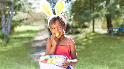 Cute African American girl eating and enjoying Easter candy wearing bunny ears