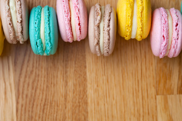 Colorful pastel macaroons on wooden table. French almond cookies, flat lay style. Macarons background, place for text.