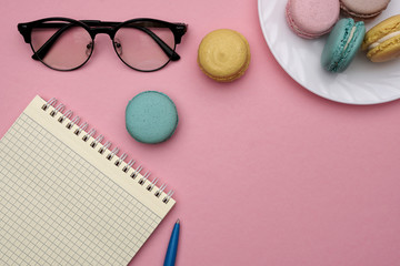 Woman's flat lay workplace with glasses, pen, notebook and pastel macaroons. Place for text.