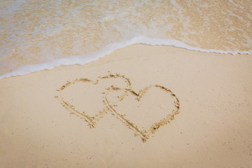 two hearts drawn on sand beach